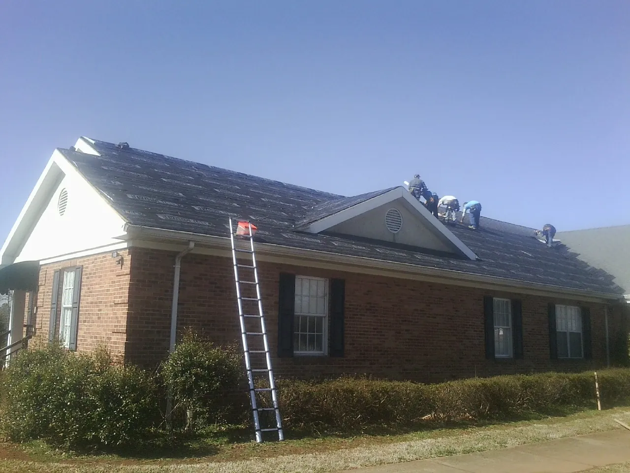 Crew tearing shingles off a brick ranch roof with a ladder set — Emergency Roof Repair work by our crew in Quincy