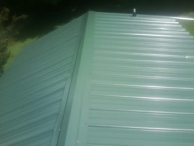 New green metal panels meeting at the ridge of a roof — Flat Roof Repair work by our crew in Quincy