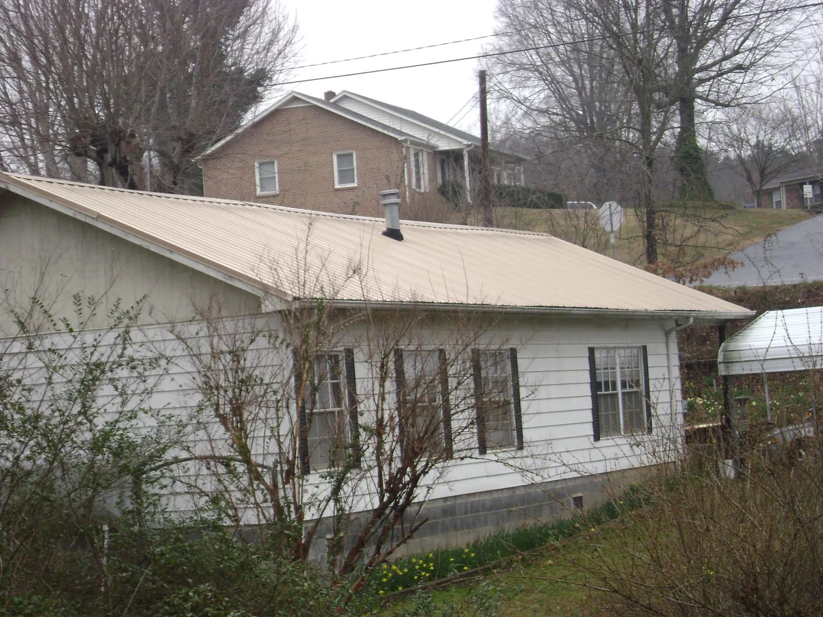 Tan metal roof on a white sided house set into a hillside — Commercial Roofing by Roofing Brothers in Quincy